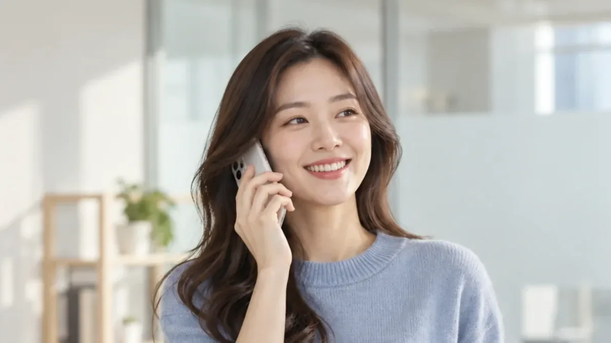 밝은 사무실에서 휴대폰으로 통화하며 웃는 여성